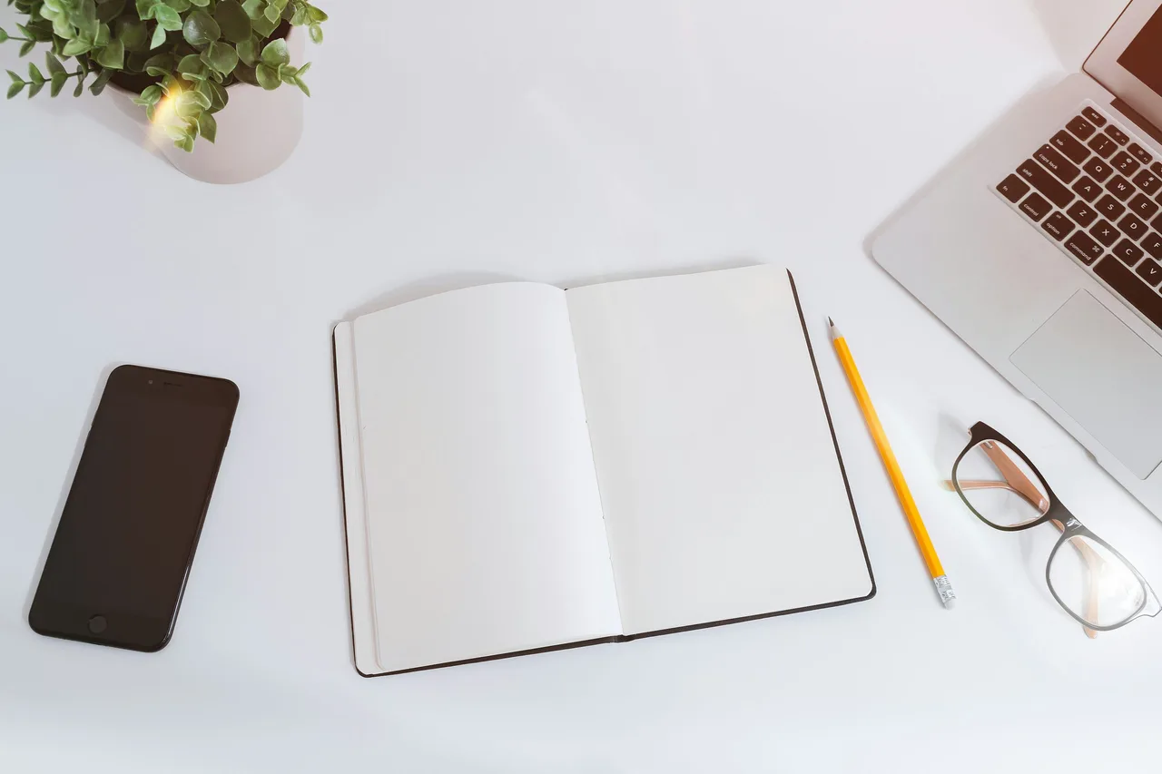 An open notebook beside a laptop, phone and pencil on a desk.
