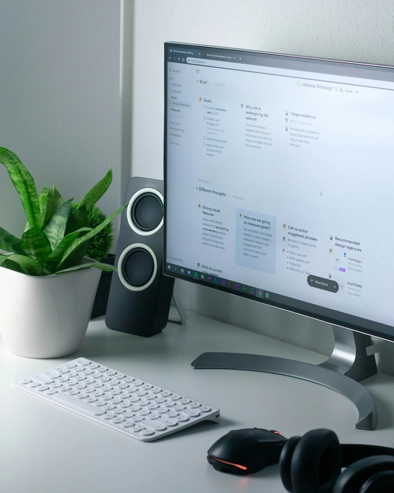 A desktop monitor displaying a workspace with notes, beside a keyboard and headphones.