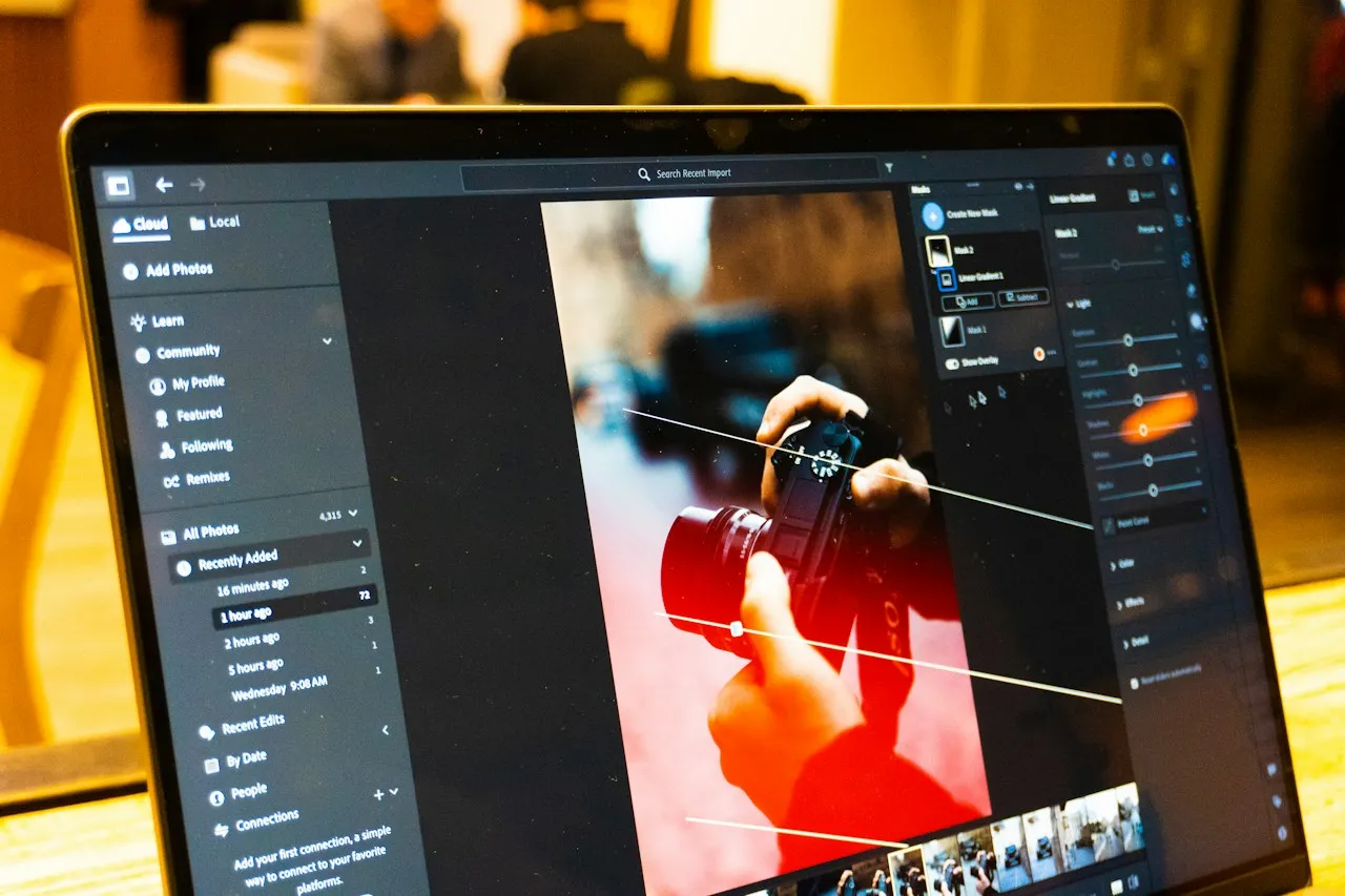 A laptop screen shows photo-editing software with an image of hands holding a camera and a panel of adjustment sliders.