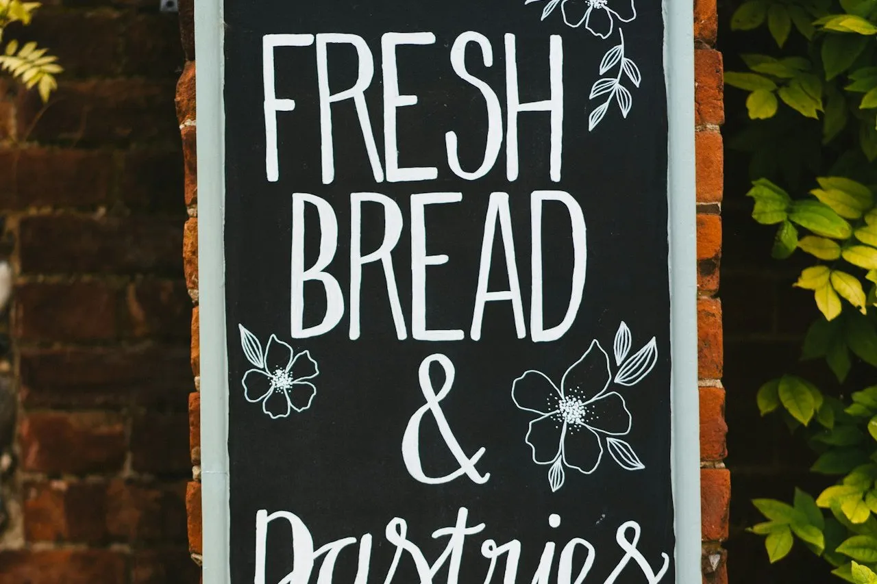 A hand-lettered blackboard sign on a brick pillar reads 'Fresh bread &' above the start of the word 'Pastries'.