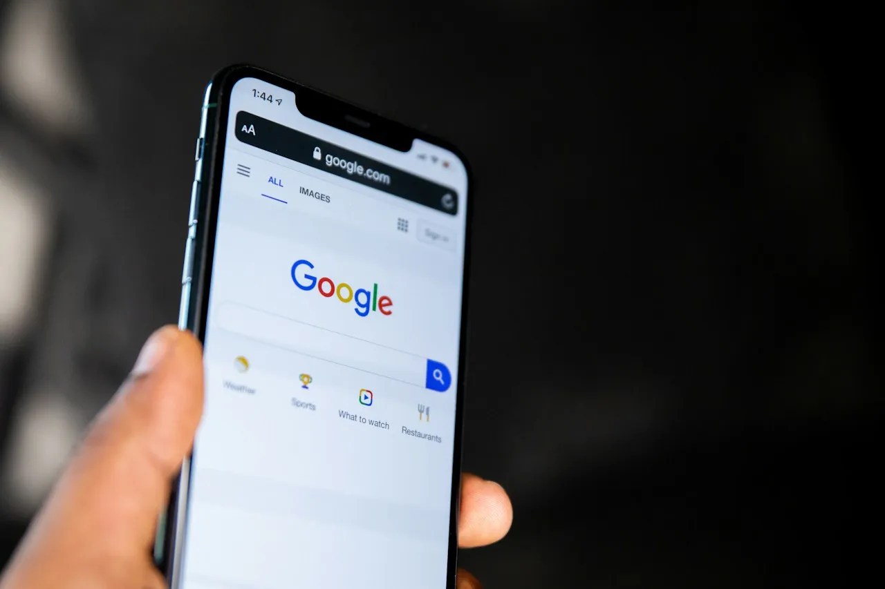 A hand holds a smartphone showing the Google search home page.
