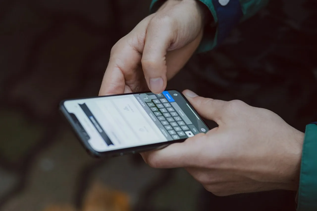 Close-up of two hands typing a message on a smartphone keyboard.