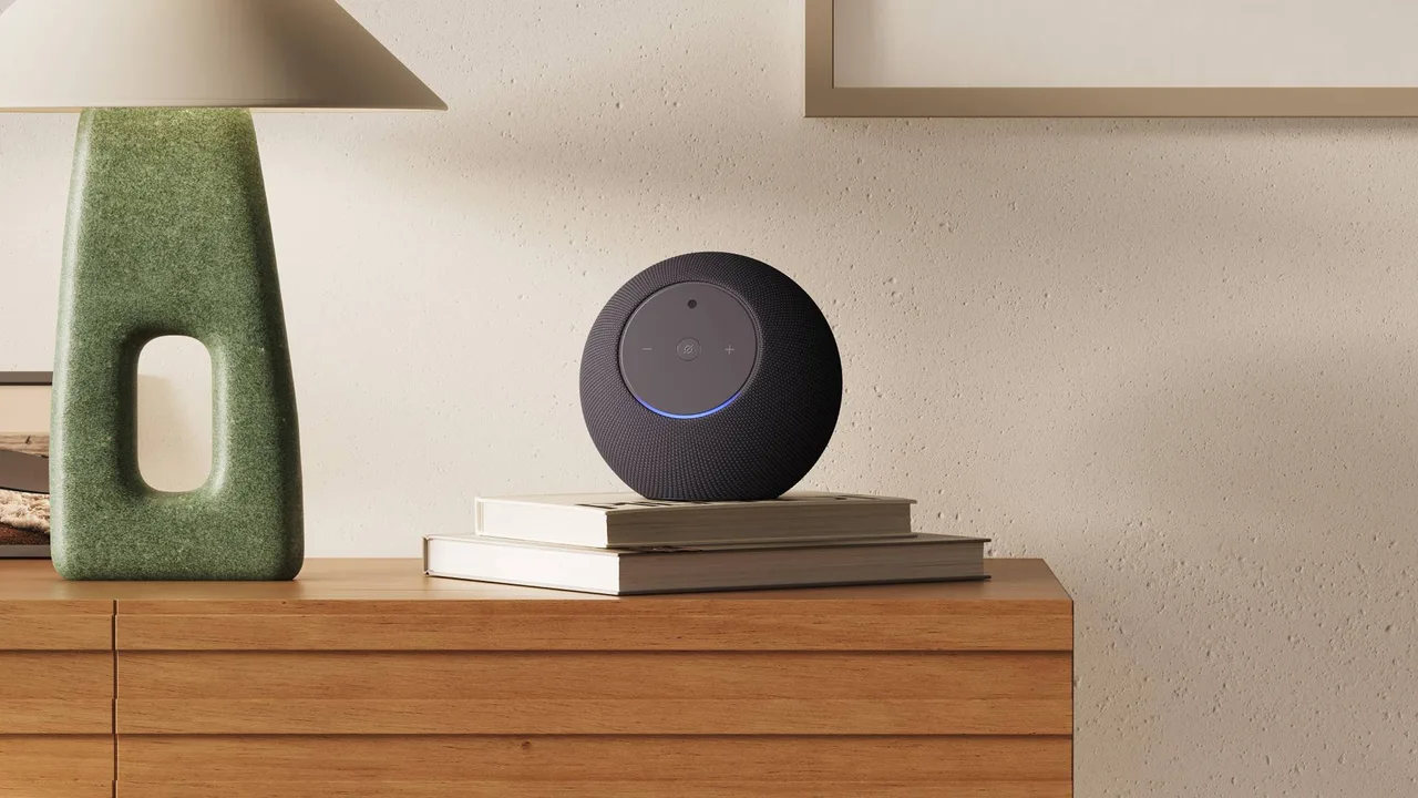 Amazon's press image of a dark grey, ball-shaped Echo Studio with Home Camera sitting on a stack of books on a wooden sideboard, with a small blue light arc at the bottom of its flat face.
