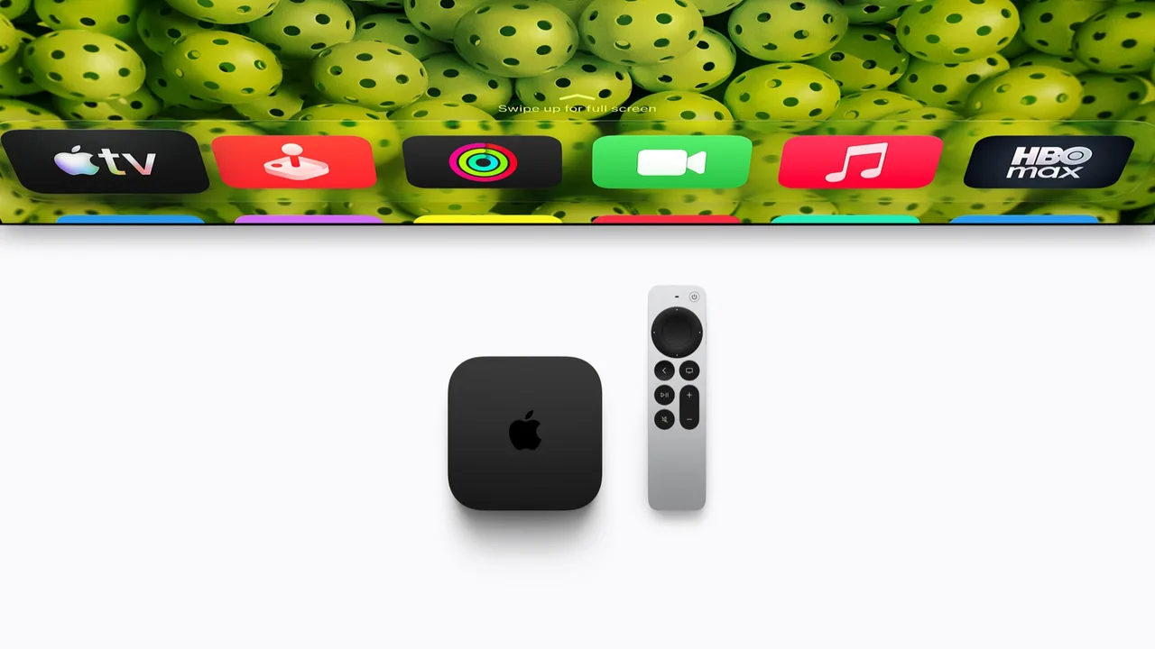 Apple's press image of the Apple TV 4K, a small black square box with the Apple logo on top, beside a silver Siri Remote. Above them is the bottom edge of a television showing a row of app icons.