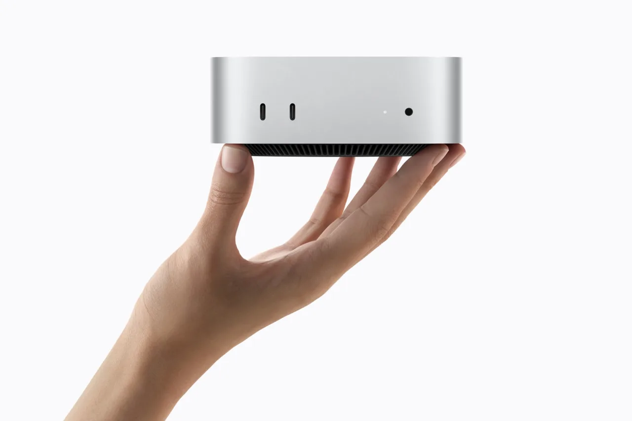 A hand holding the new Mac mini, showing its two front USB-C ports, status light and headphone jack.
