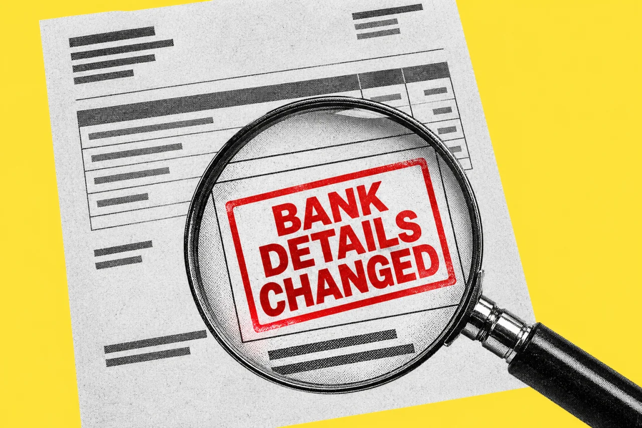 An invoice with a large magnifying glass over its bank details, on a yellow background. Inside the magnifying glass a bold red stamp reading "BANK DETAILS CHANGED".